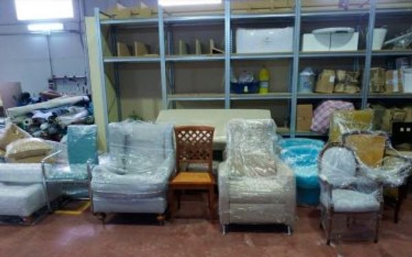 Taller de tapicería con varios sillones, una silla y un sofá recién tapizados, protegidos con plástico